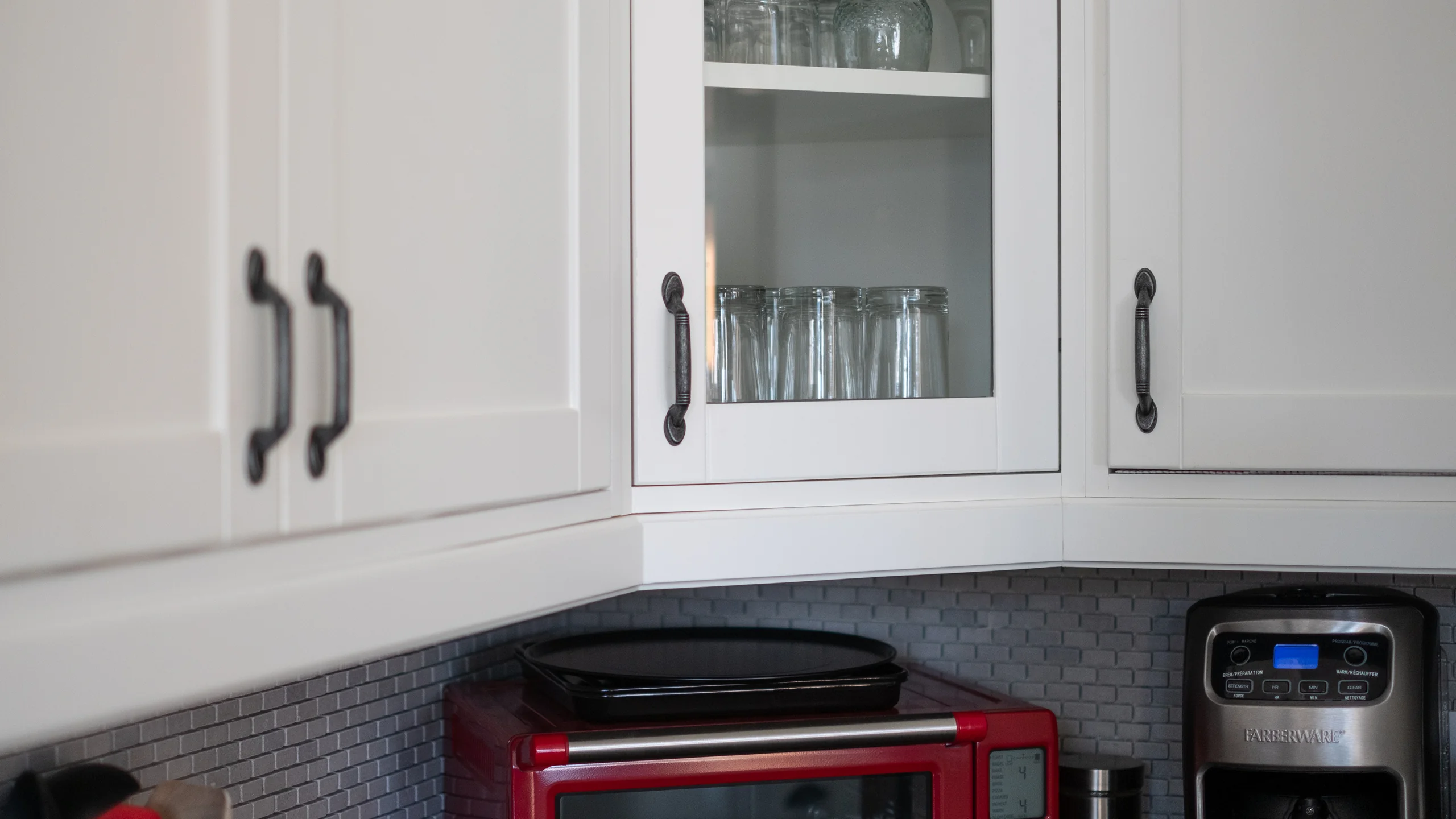 Upper cabinetry with glass-front display and dark mosaic backsplash