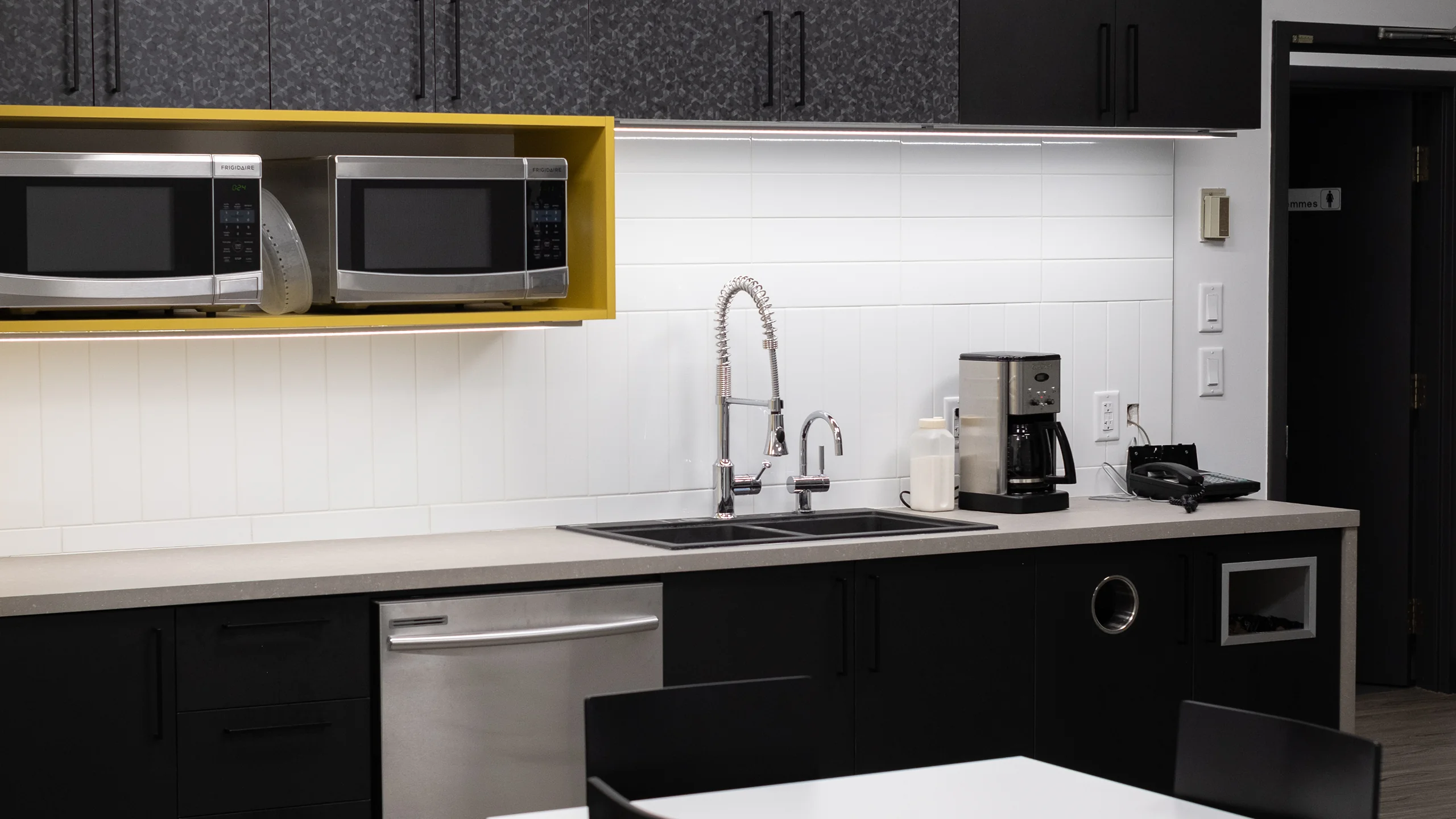 Breakroom kitchen with bold yellow open shelving and double-basin sink