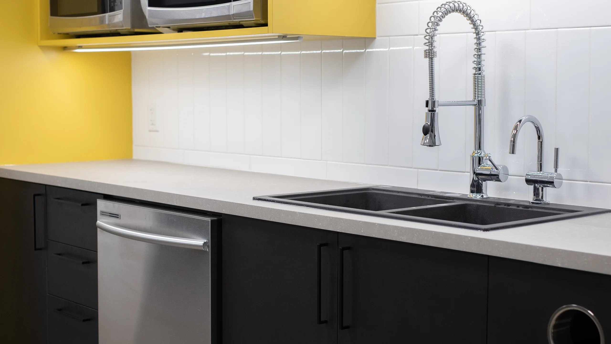 Yellow upper cabinetry with dual microwaves above double-basin sink